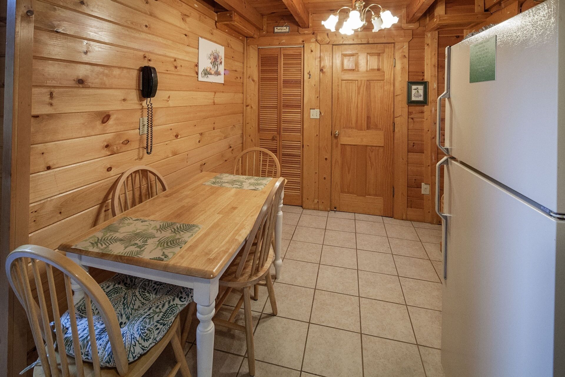 A wooden interior with a dining table, chairs, a refrigerator, and a telephone.