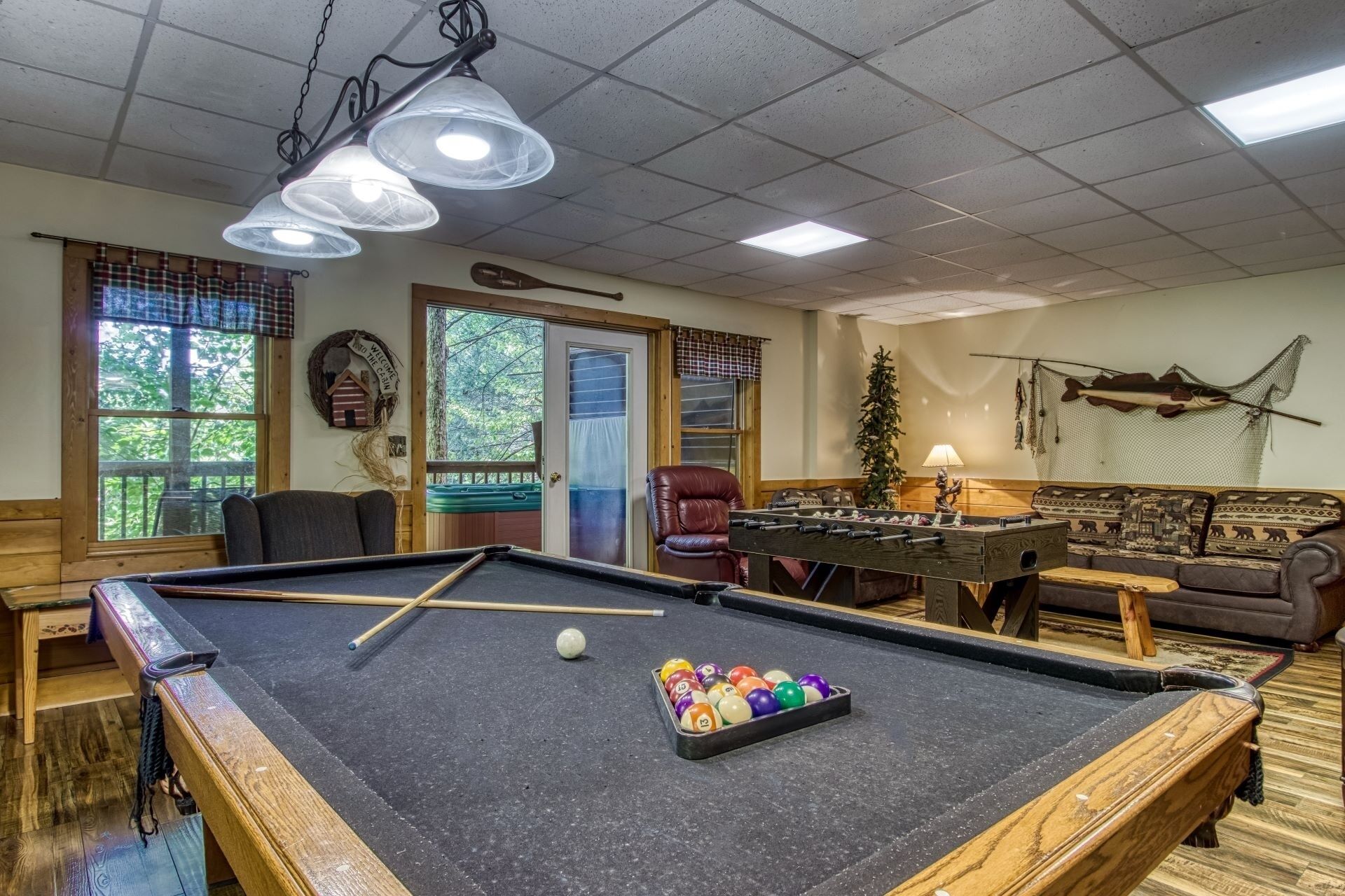A pool table with balls, a foosball table, a sofa, and a door leading outside.