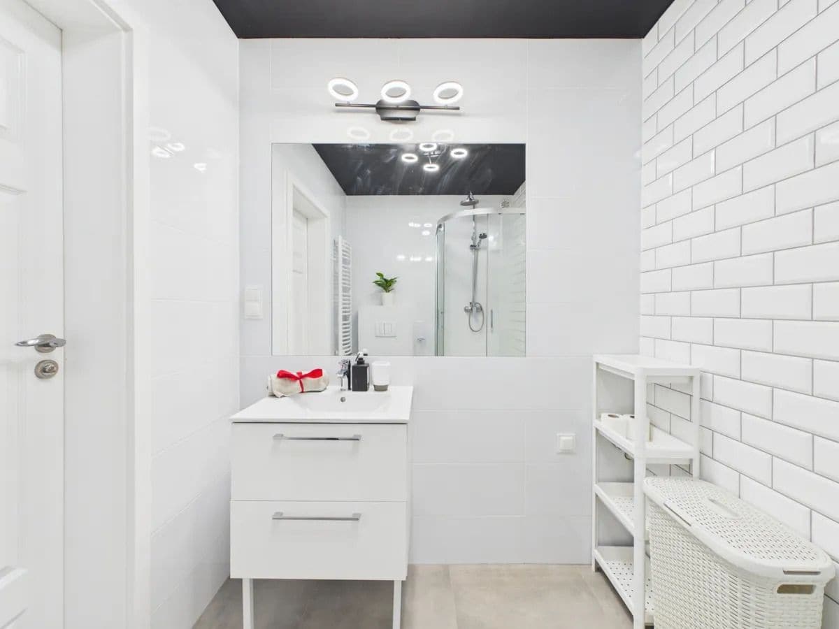 A modern bathroom with a white sink, mirror, and shelving unit.