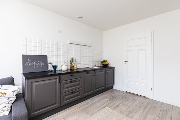 A modern kitchen with dark grey cabinets, a black countertop, and white tiled backsplash. - Super Apart Obywatelska (Warsaw)