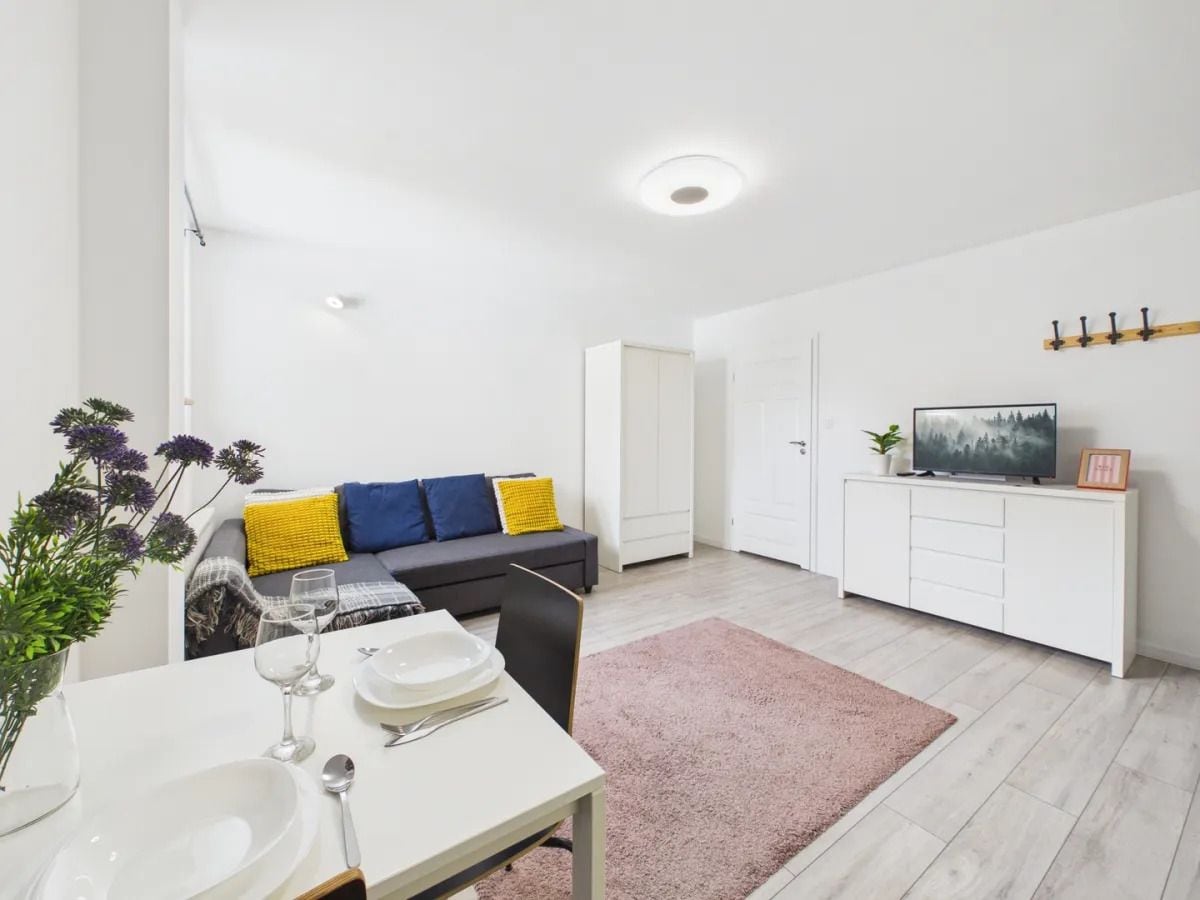 Un espacio habitable moderno con comedor, un sofá con cojines, un televisor sobre un mueble y una planta.