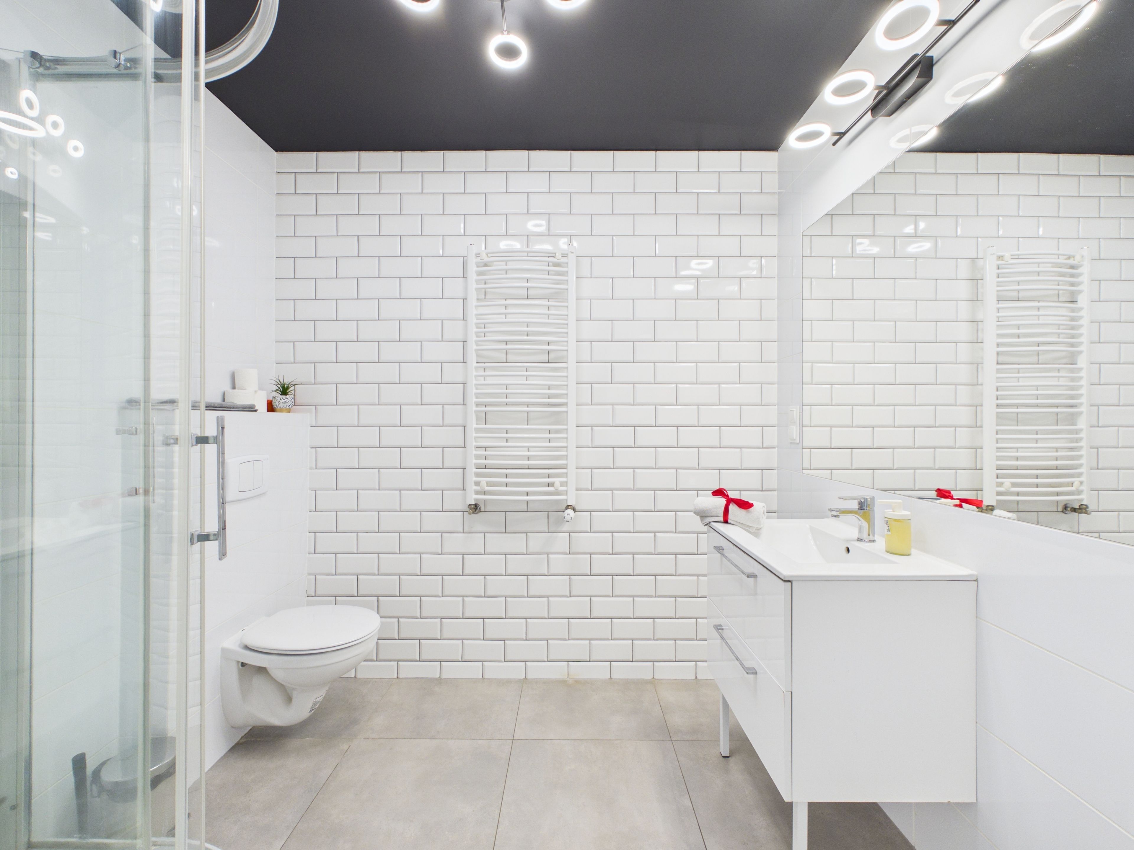 Un bagno moderno con piastrelle bianche tipo metro, box doccia in vetro, vaso WC bianco e mobile lavabo con specchio.