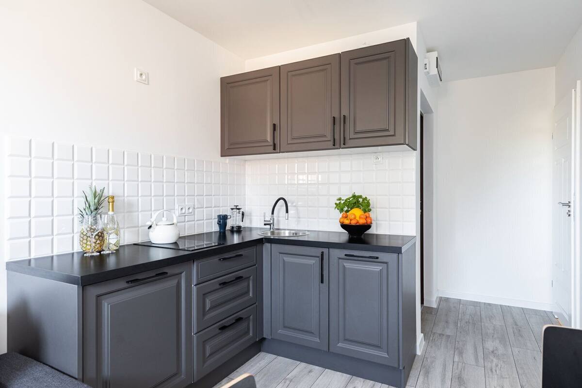 Una cocina moderna con gabinetes grises, encimera negra, salpicadero de azulejos blancos y un frutero en la encimera.
