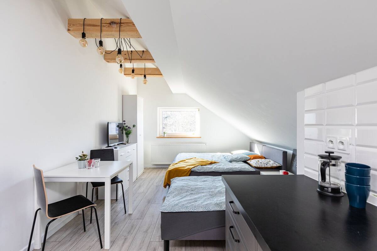 Un dormitorio moderno con una cama alta, un escritorio y una kitchenette.