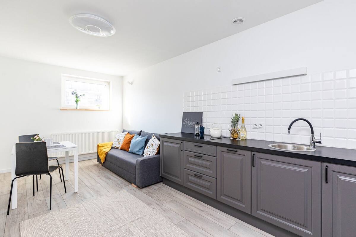 Una cocina moderna con armarios grises, una encimera negra y un salpicadero blanco de azulejos.
