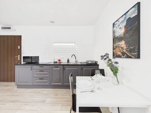 A modern kitchen with grey cabinets, a white countertop, and a dining area with a white table set for two. - Super Apart Obywatelska (Warsaw)