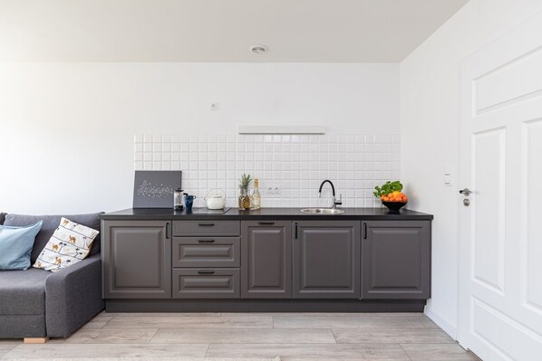 A modern kitchen with grey cabinets, a white tiled backsplash, and a black faucet.