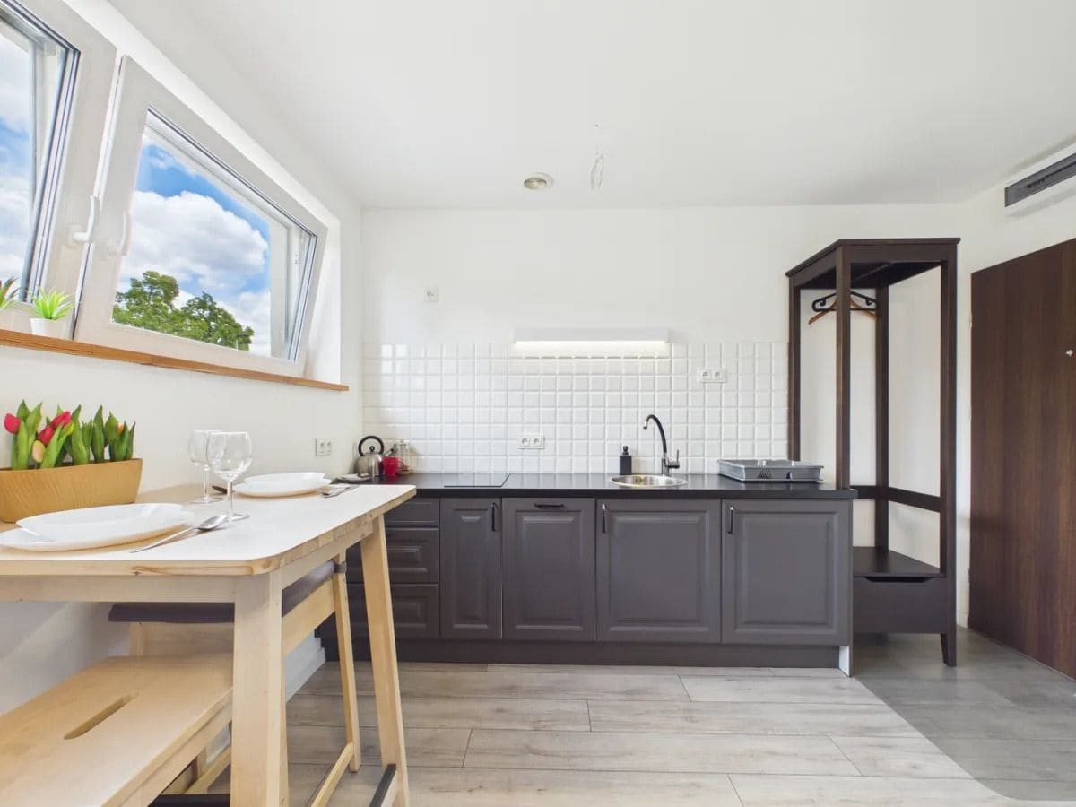 Una cocina moderna con una mesa de madera, armarios oscuros y una ventana con vistas a árboles.