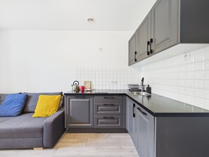 A modern kitchen with grey cabinets, a black countertop, and a white tiled backsplash. - Super Apart Obywatelska (Warsaw)