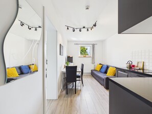 A modern kitchen with a dining area, a sofa with cushions, and a window with a view of greenery. - Super Apart Obywatelska (Warsaw)