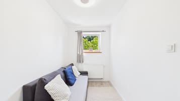 Una habitación moderna y minimalista con un sofá gris, un radiador blanco y una ventana con vistas a zonas verdes.