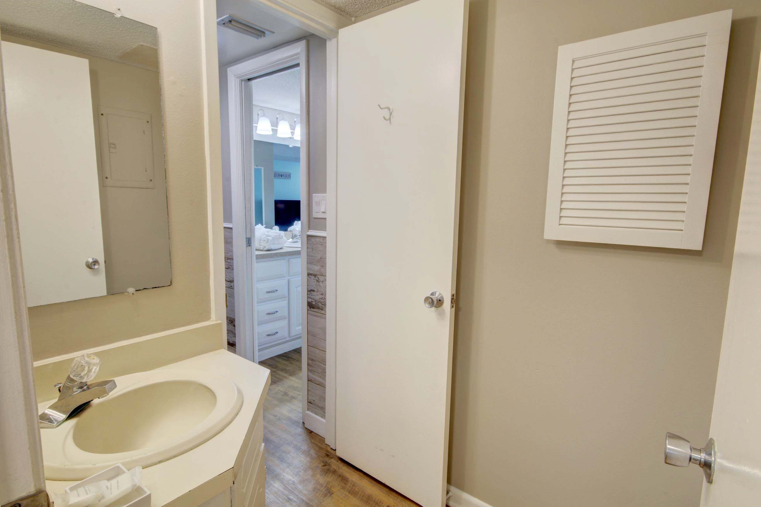 A bathroom with a sink, mirror, and a door leading to a bedroom.