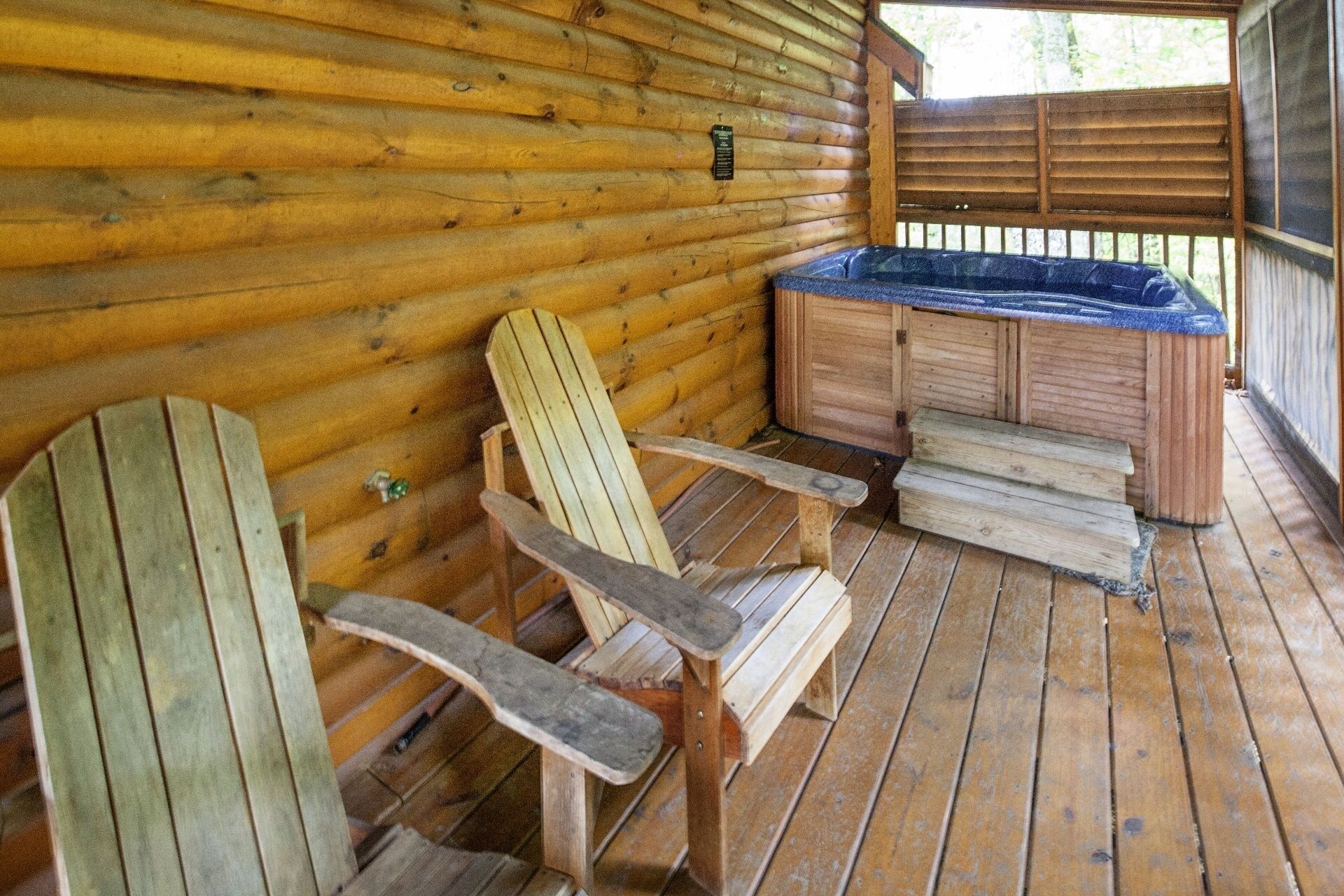 Eine Holzhütte mit Whirlpool, zwei Adirondack-Stühlen und einer Holzterrasse.
