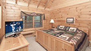 A cozy wooden cabin room with a bed, a desk, a television, and a window with blinds. - Er314- Y'all Come Back Now- Great Location- Close To Town 2 Bedroom Cabin by RedAwning (Pigeon Forge)
