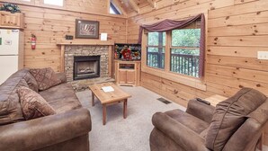 A cozy cabin interior with a stone fireplace, wooden walls, a sofa set, and a television. - Er314- Y'all Come Back Now- Great Location- Close To Town 2 Bedroom Cabin by RedAwning (Pigeon Forge)