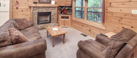 Un intérieur de chalet chaleureux avec une cheminée en pierre, des murs en bois, un ensemble de canapés et un téléviseur.