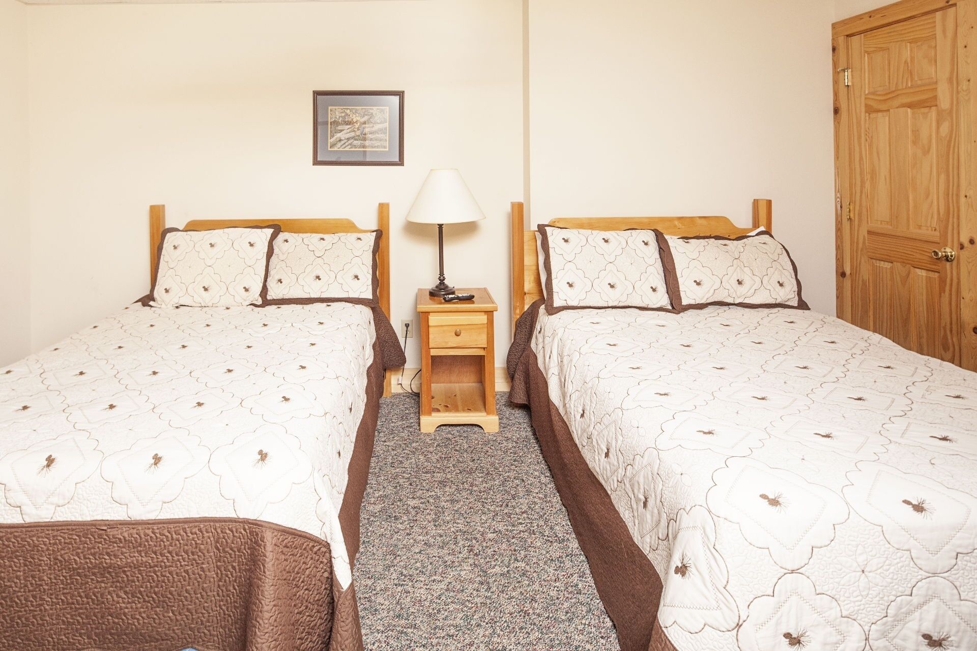 A room with two single beds, a nightstand with a lamp, a framed picture on the wall, and a wooden door.