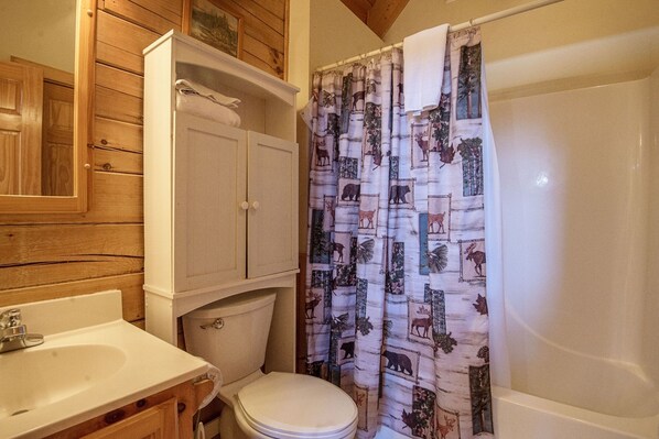 Un baño con tocador de madera, inodoro y cortina de ducha con estampados de animales.