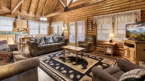 Ein Blockhaushaus-Interieur mit einem Holztisch, einer Couch, Sesseln und einem Teppich mit Tiermustern.