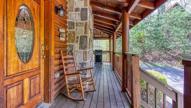 Eine hölzerne Veranda mit einer Steinmauer, einem Schaukelstuhl und einem Grill.