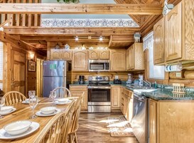 A wooden cabin-style kitchen with a dining area, featuring a refrigerator, stove, microwave, and wooden cabinets.