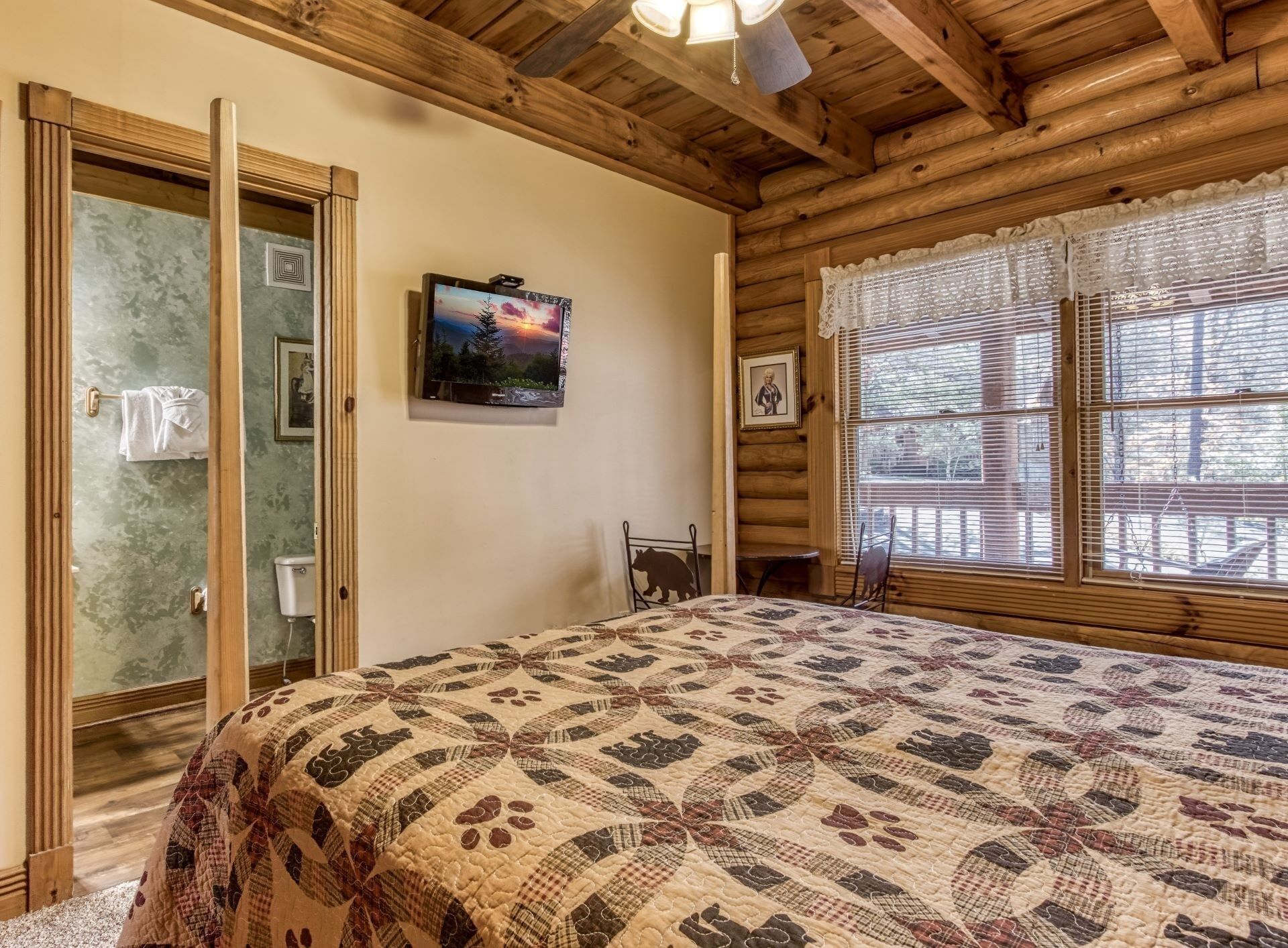 A cozy log cabin room with a large bed, a television, and a window with blinds.