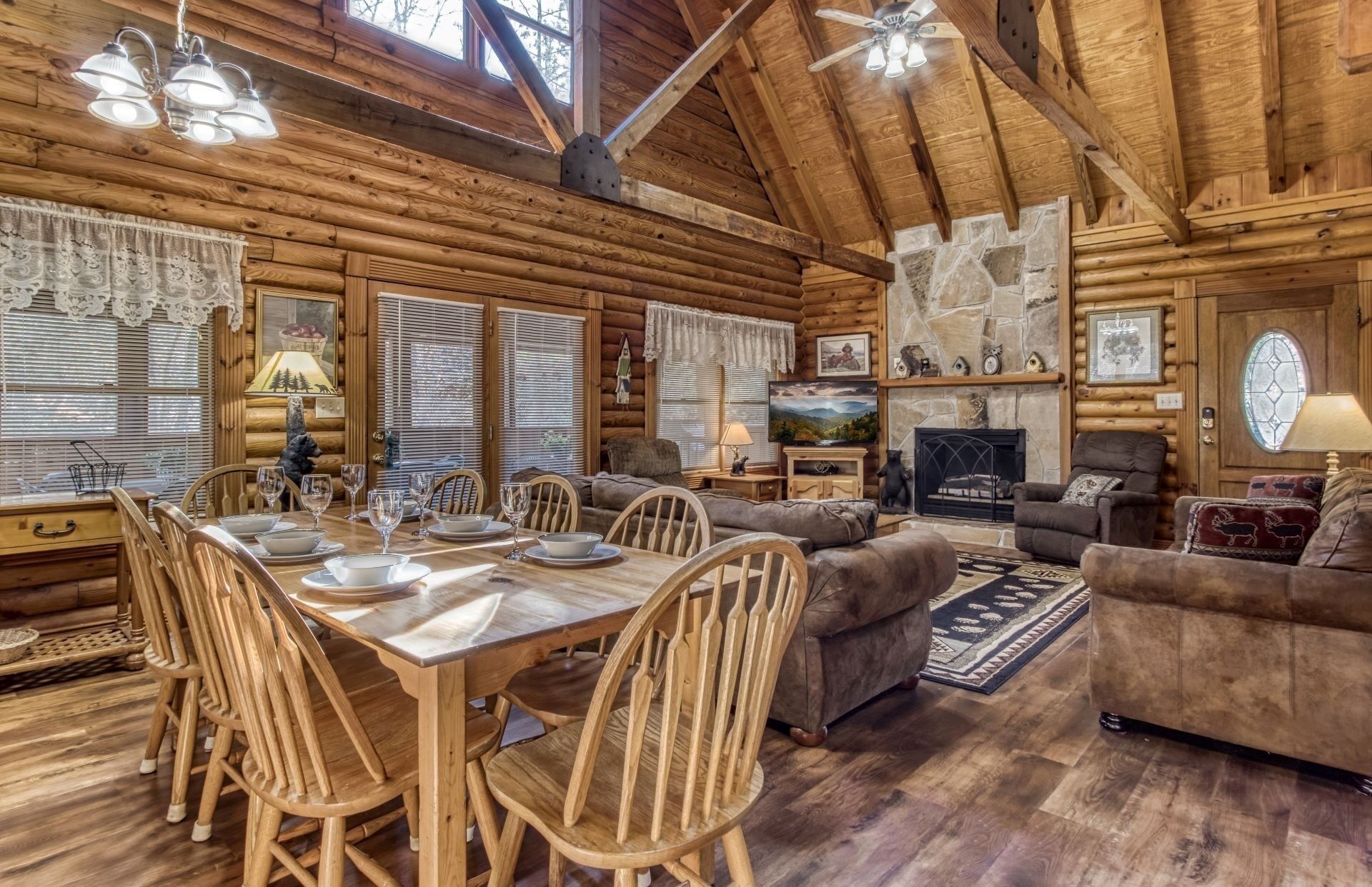 A log cabin interior with a dining area, sofas, a fireplace, and a stone wall.