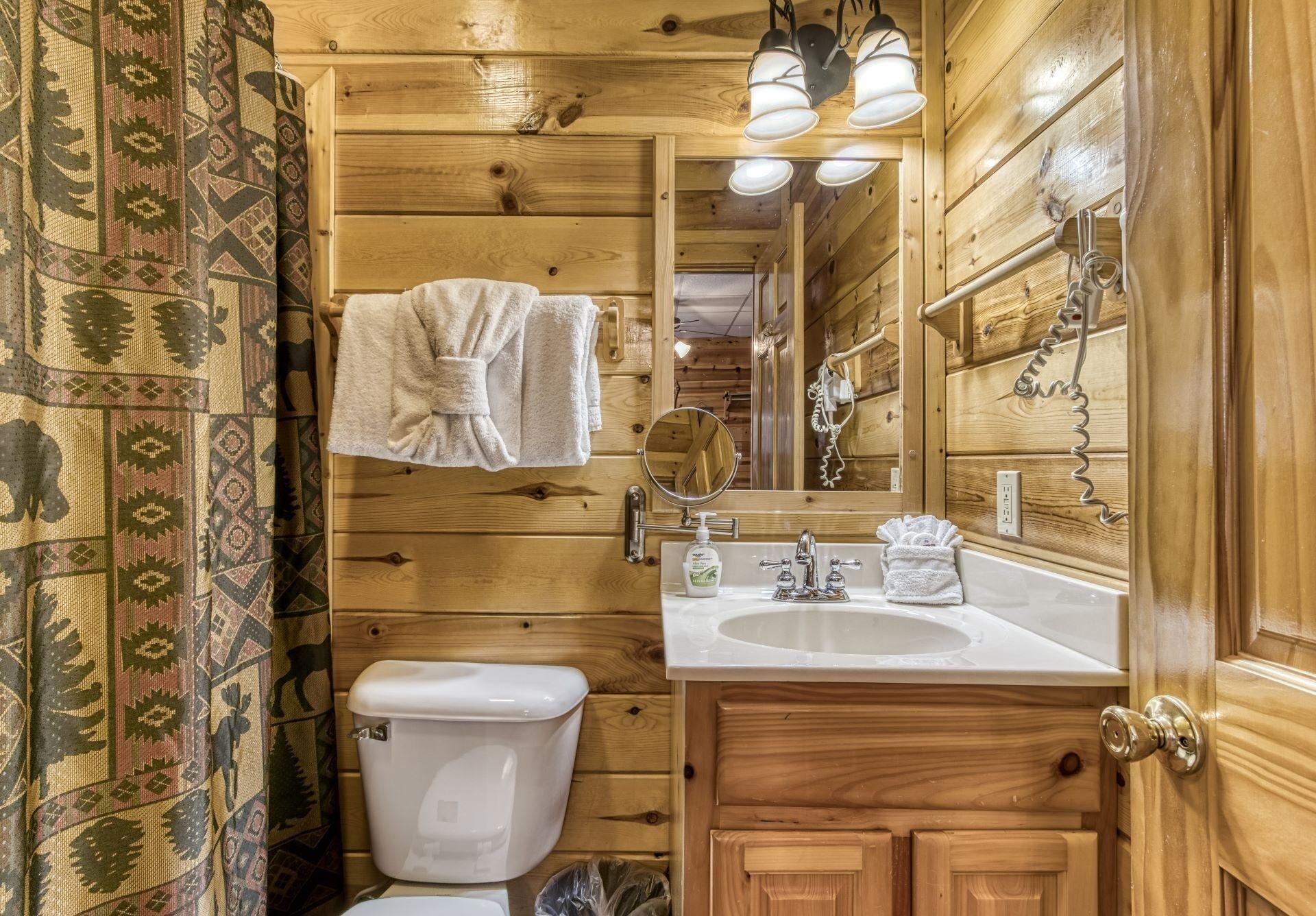 A wooden bathroom with a toilet, sink, and mirror.