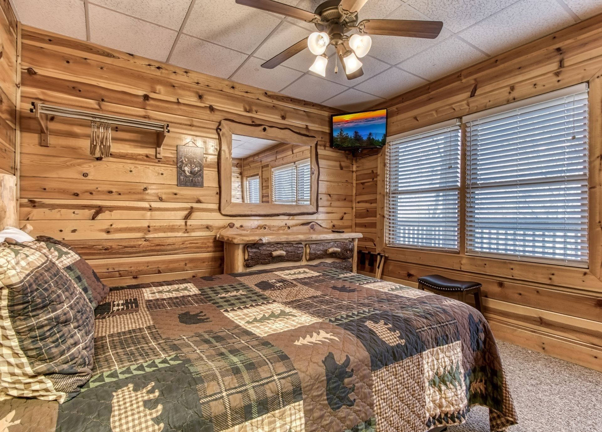 A log cabin room with a bed, a TV, a mirror, and a window with blinds.