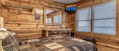 A log cabin room with a bed, a TV, a mirror, and a window with blinds.