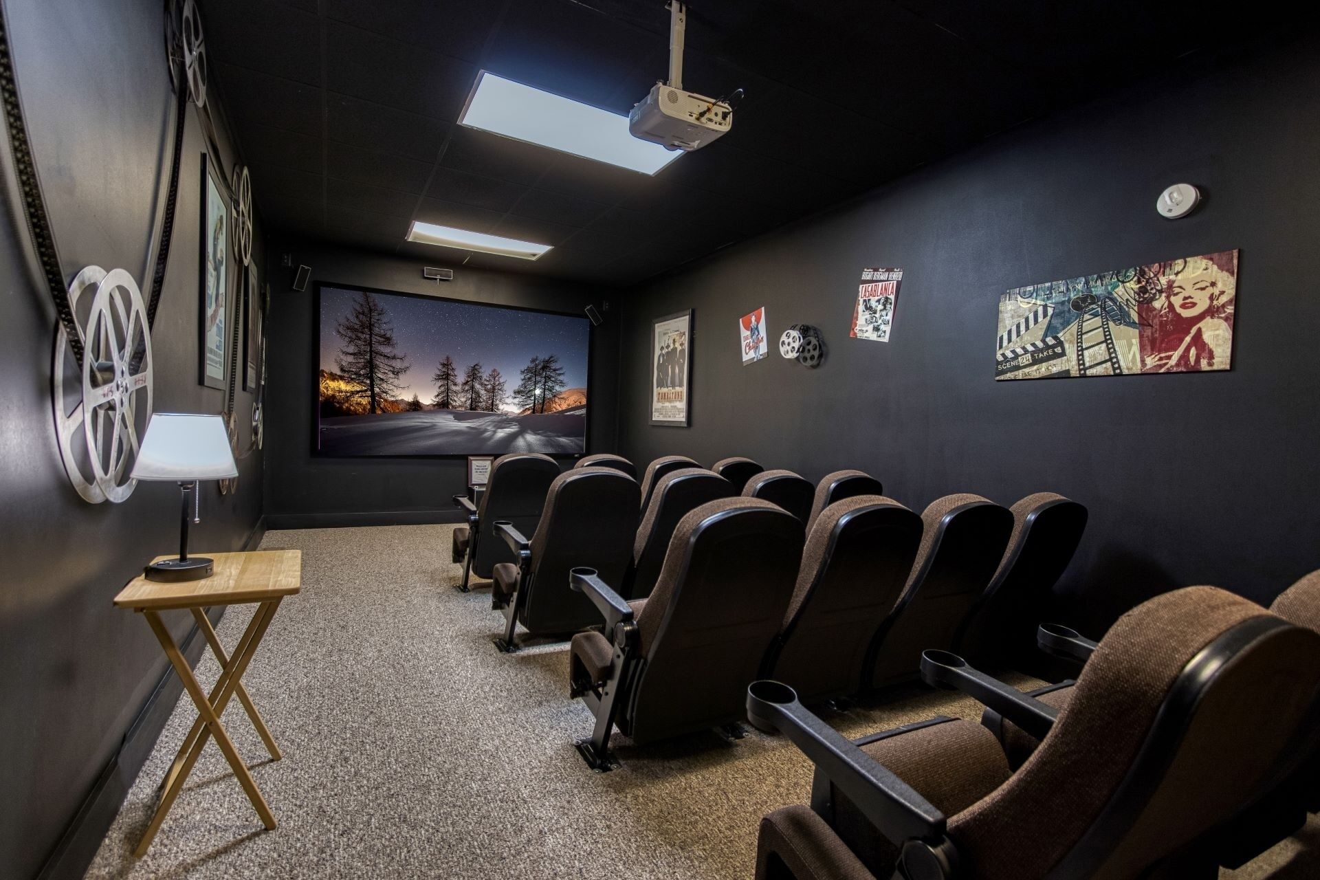 Une salle de cinéma privée équipée d’un grand écran, de fauteuils inclinables, d’un projecteur et de plusieurs affiches de films accrochées au mur.
