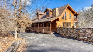 A log cabin with a stone wall, a wooden deck, and a clear sky. - The Wildlife Lodge - Great Location! Close To Tanger Outlets! 5 Bedroom Cabin by RedAwning (Sevierville)