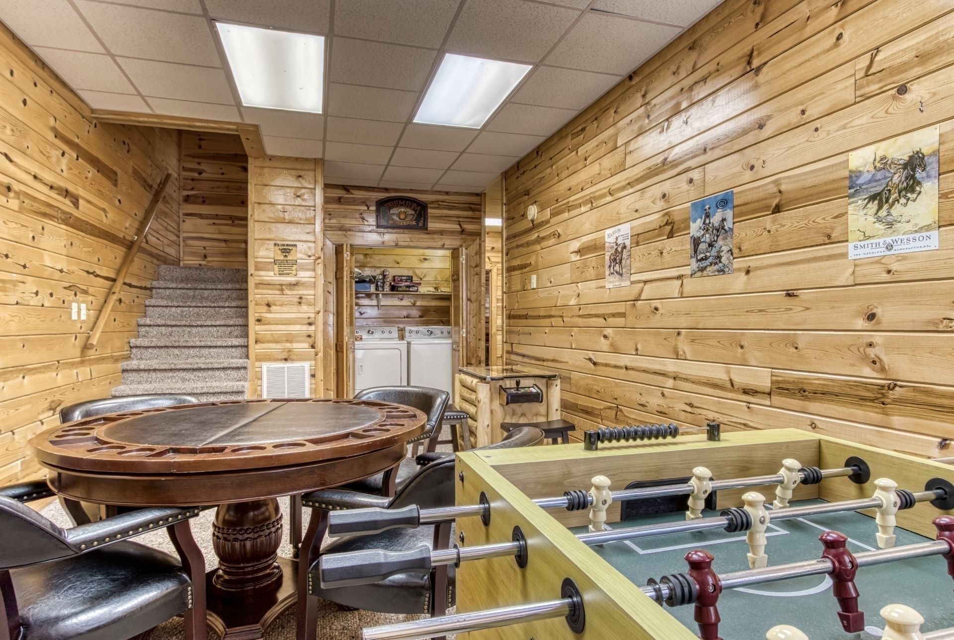 Una habitación acogedora con detalles de madera, una mesa de fútbol de mesa, una mesa con sillas y una escalera que lleva a una zona de cocina.