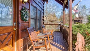 A wooden cabin with a porch, two wooden chairs, and a wreath on the door. - Er83 - Savage Loft - Your Close To The Action Cabin Getaway 2 Bedroom Cabin by RedAwning (Pigeon Forge)