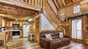A cabin interior with a kitchen, dining area, and a staircase leading to a loft. - Er83 - Savage Loft - Your Close To The Action Cabin Getaway 2 Bedroom Cabin by RedAwning (Pigeon Forge)