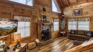A cozy cabin interior with a fireplace, wooden walls, a sofa, and a Christmas tree. - Er83 - Savage Loft - Your Close To The Action Cabin Getaway 2 Bedroom Cabin by RedAwning (Pigeon Forge)