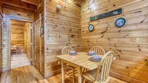 A wooden cabin interior with a dining table set for four, a "Welcome" sign, and a "Cabin" sign on the wall.