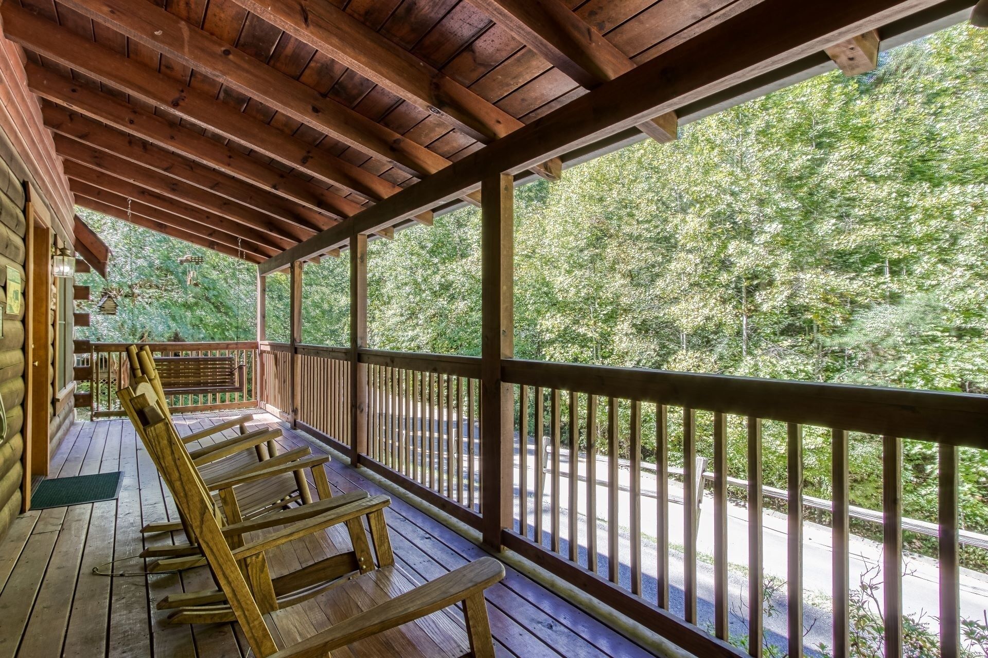 A wooden deck with benches, a covered area with a wooden ceiling, and a view of a forested area.