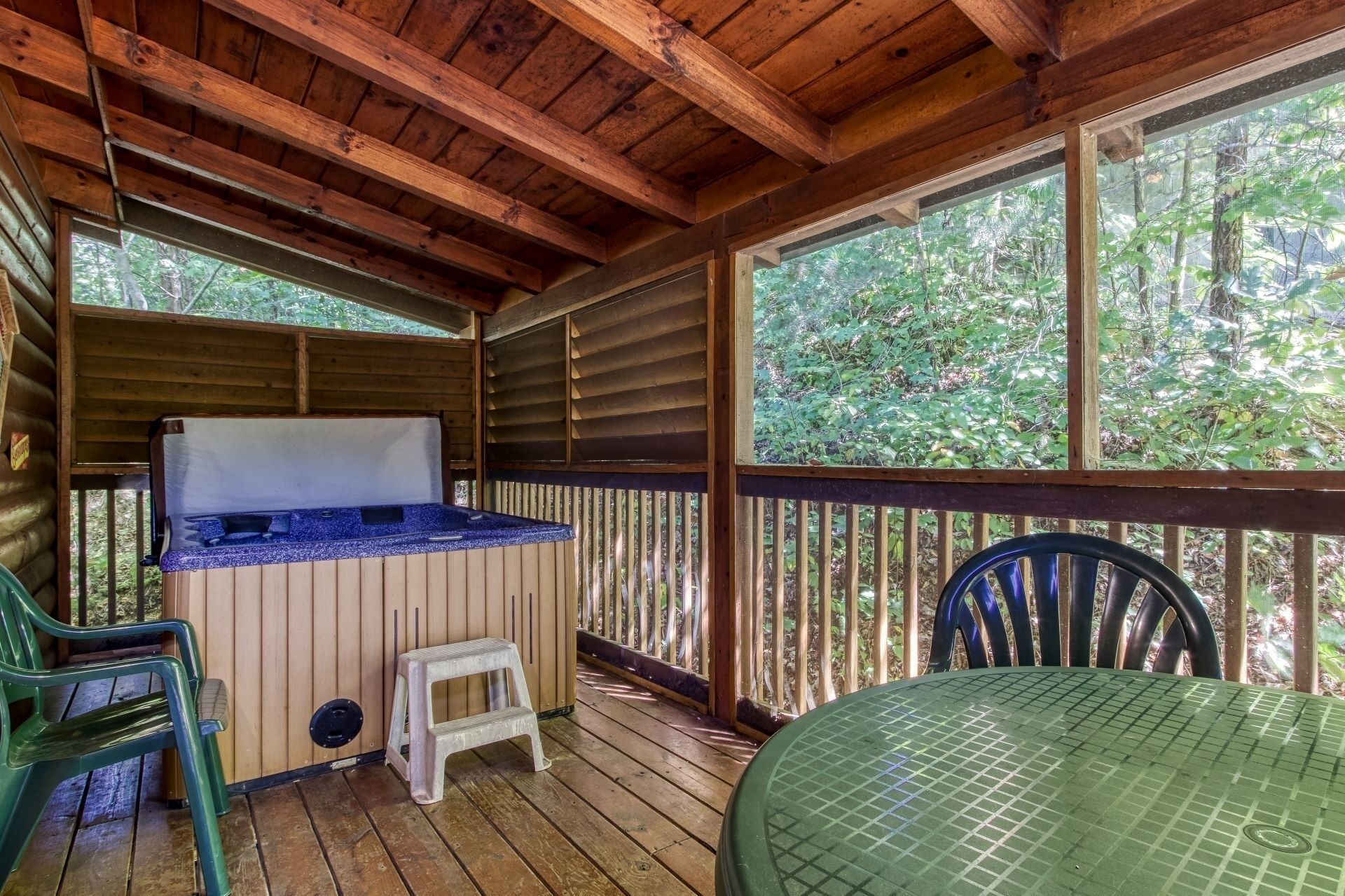 A covered outdoor area with a hot tub, a small stool, and a table.