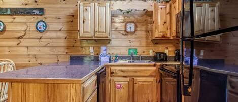 A wooden cabin-style kitchen with wooden cabinets, a black refrigerator, and a clock on the wall.