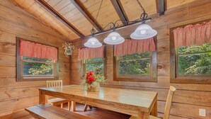 A wooden cabin interior with a dining table, benches, and large windows with red curtains. - Er309- George's- Great Location- Close To Town 5 Bedroom Cabin by RedAwning (Pigeon Forge)