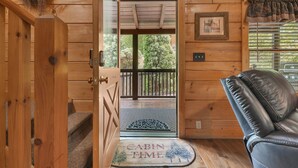 A wooden cabin interior with a door leading to a balcony, a leather chair, and a welcome mat. - Er309- George's- Great Location- Close To Town 5 Bedroom Cabin by RedAwning (Pigeon Forge)