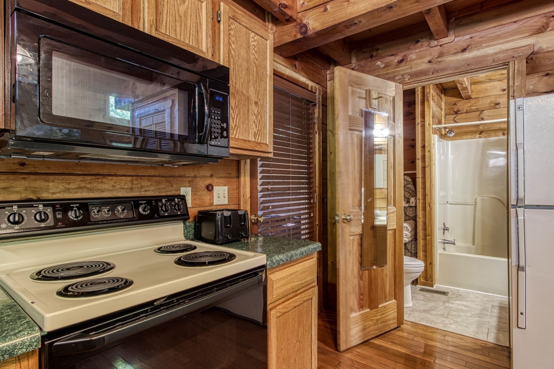 A compact kitchen with a microwave, stove, toaster, and wooden cabinets.