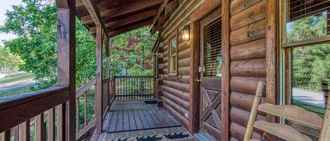 A wooden cabin with a porch, a wooden bench, and a rug with animal designs.