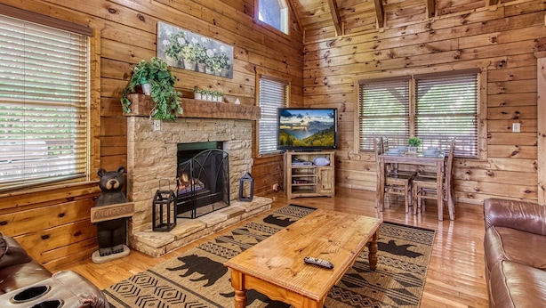 Un intérieur de chalet chaleureux avec une cheminée en pierre, des murs en bois, un téléviseur et un coin repas.