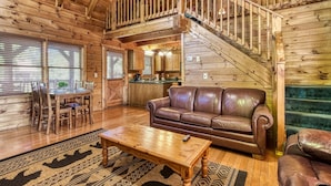 Un intérieur de chalet en bois spacieux, comprenant un coin repas, un canapé en cuir et un escalier menant à un niveau supérieur.