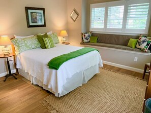A neatly arranged bedroom with a bed, bedside lamps, a window with blinds, a bench with cushions, and a rug. - Olde Beau Cottage MAGNIFICENT VIEWS! (Glade Valley)