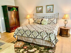Ein Schlafzimmer mit einem Bett, zwei Nachttischlampen, einem Nachttisch, einem Holzschrank und zwei gerahmten Bildern an der Wand.