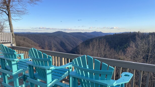 Une terrasse avec des fauteuils Adirondack turquoise donnant sur un paysage montagneux.