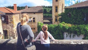 Dos personas observan un pueblo histórico con edificios de piedra y una torre.